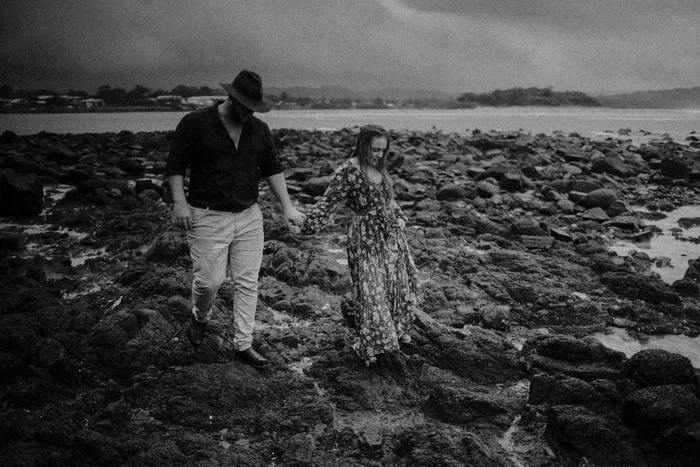 A couple walking across wet rocks at the edge of the ocean